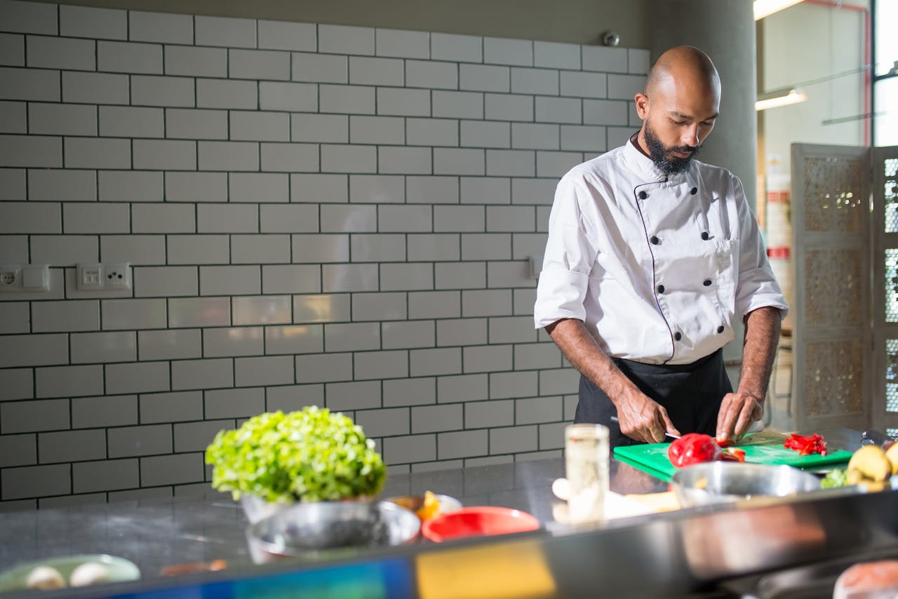 A skilled chef in a white uniform slices fresh vegetables on a chopping board in a modern kitchen.