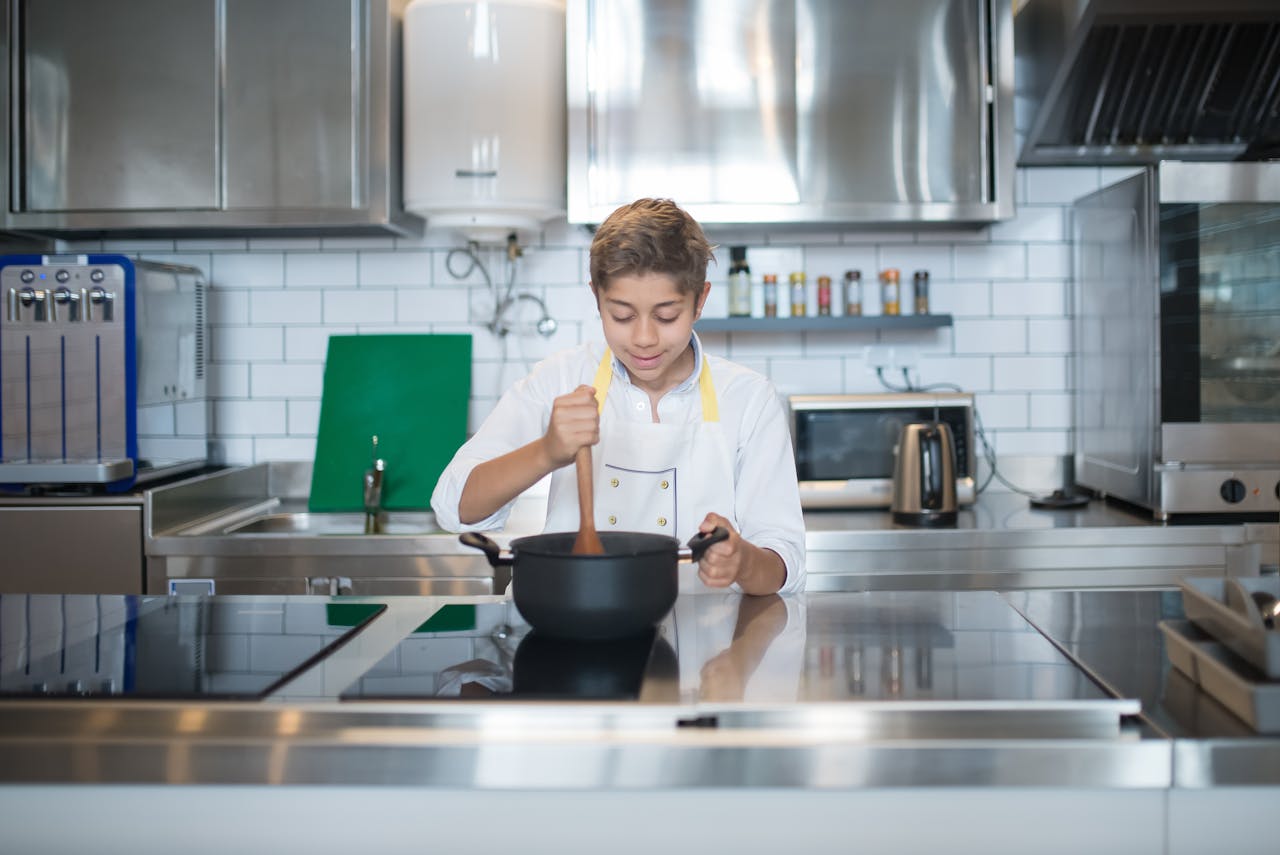 An aspiring young chef in an apron cooks with focus in a sleek, modern kitchen setting.