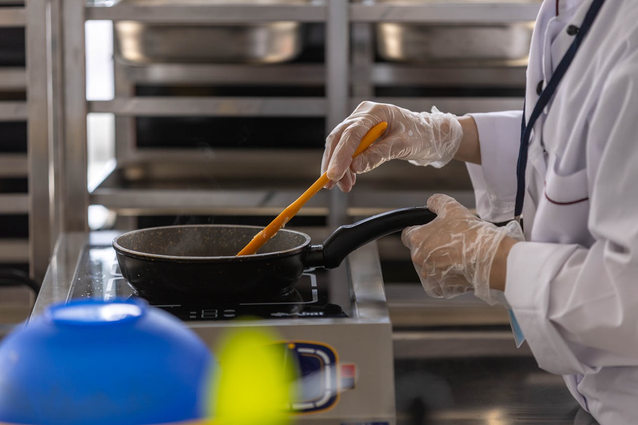 Chef in professional kitchen cooking with frying pan using stovetop.